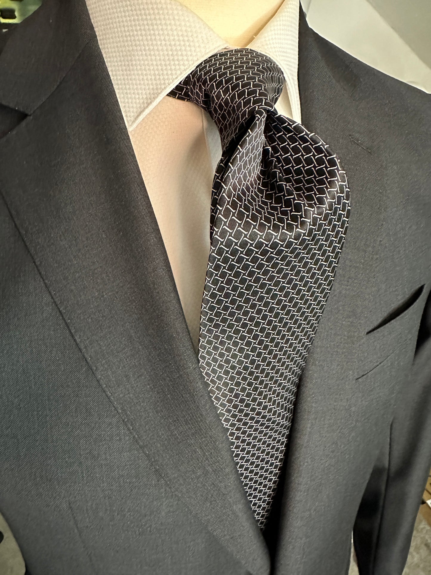 This satin finish 100% silk necktie has a very interesting all over geometric pattern of interlocking white links almost chain link in style. The silk is very smooth to the touch and has a natural luster that shines in certain light. This is a serious tie. Great for those business meetings, court dates, dinners, evening events and all around more formal attire. This is best paired with a fancy white or tone on tone white dress shirt.
