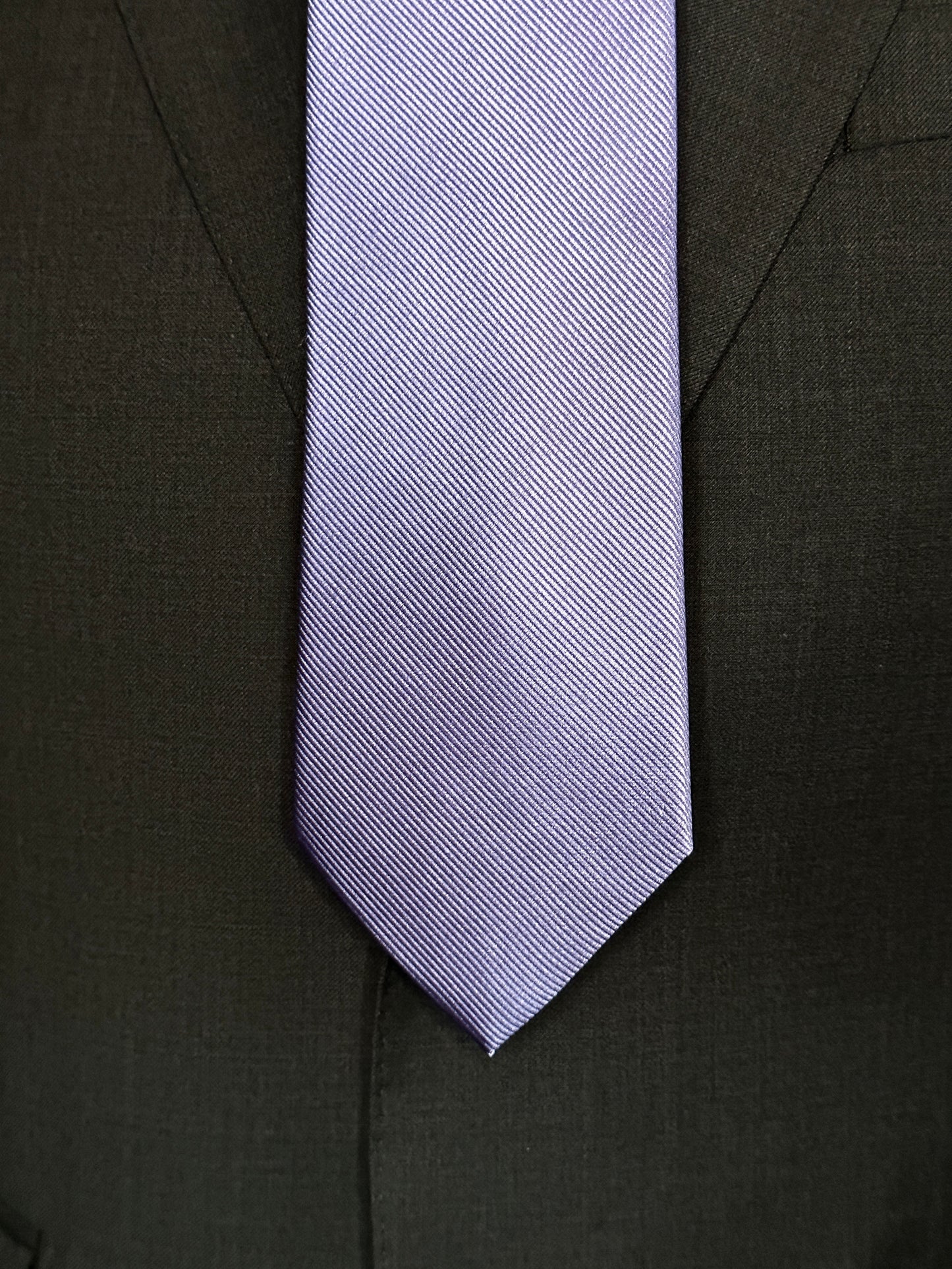 Solid ties are beautifully paired with the more busy of patters of bold stripes and heavy plaids. However, there is something so understated and elegant about a solid tie with a solid suit. Whether that be navy, charcoal or black a lavender tie fits well with a white shirt and even a navy blazer with jeans.