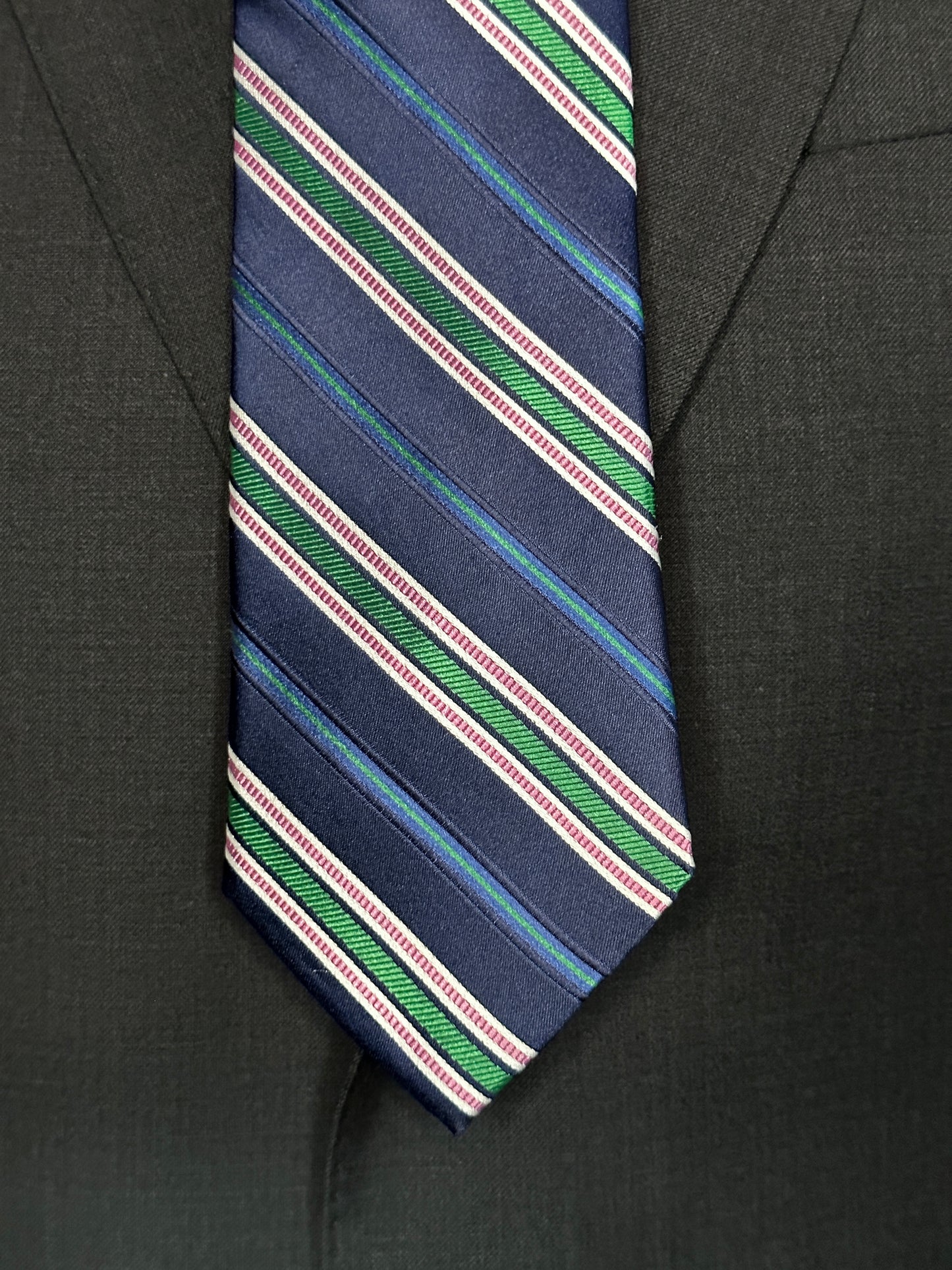 A multistripe tie has many functions. This 100% silk navy blue base tie has multiple types of stripes running through it. Light blue, rose, white ands green impact this toe in different widths. The multistripe tie allows for many types of colorations and patterns in shirts and suits. Probably the most versatile.