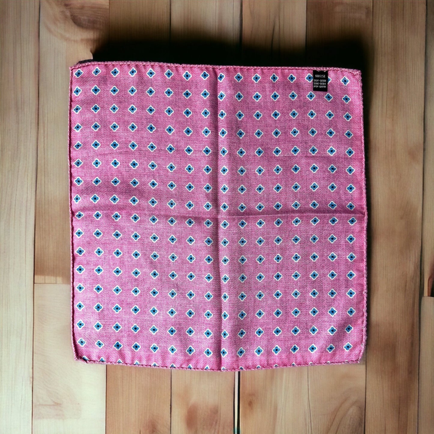 Hand rolled edges on this silk pocket square create gorgeous points that keep their position when using the breast pocket on a jacket. The pale pink and light blue circular pattern is a stunning classic all around geometric design. On the reverse is a different fun pattern of different colorful florets of blue on pink. A fun and playful pocket square for every occasion.