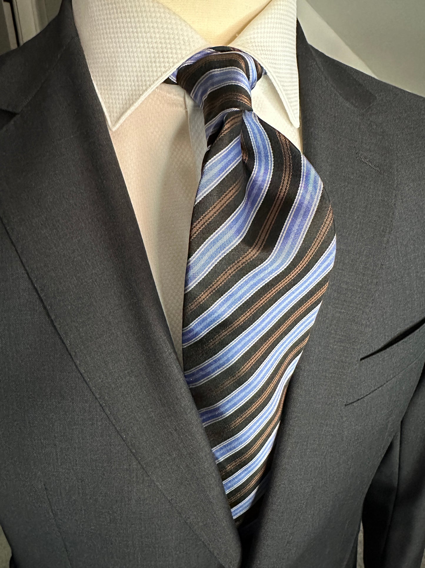 A wonderful 100% silk woven tie in clean stripes. Here we have a complimentary mixture of colors from brown and black with baby blue and white. This tie is a great business tie and would look great paired with many suit variations from black, navy, charcoal and pinstripes as well. Suits with windowpanes always do well with striped neckwear.