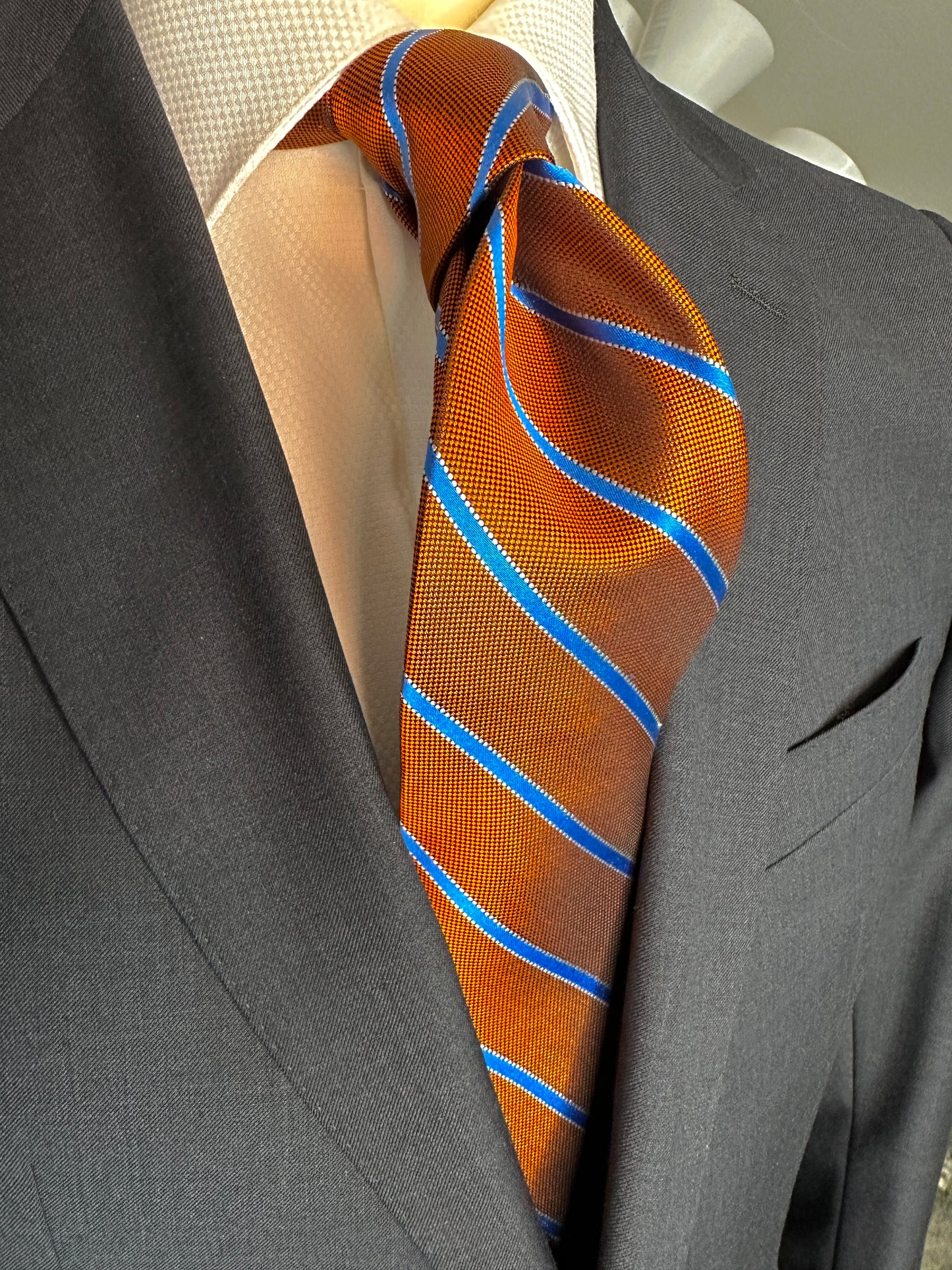 This beautiful burnt orange woven silk necktie is a stunning rich color with a baby blue stripe running through it. A perfect tie for any season and matching with a multitude of suit colors and patterns, this is a very versatile tie. In Italy, the mini plaid shirt with striped tie is a sophisticated ensemble. 
