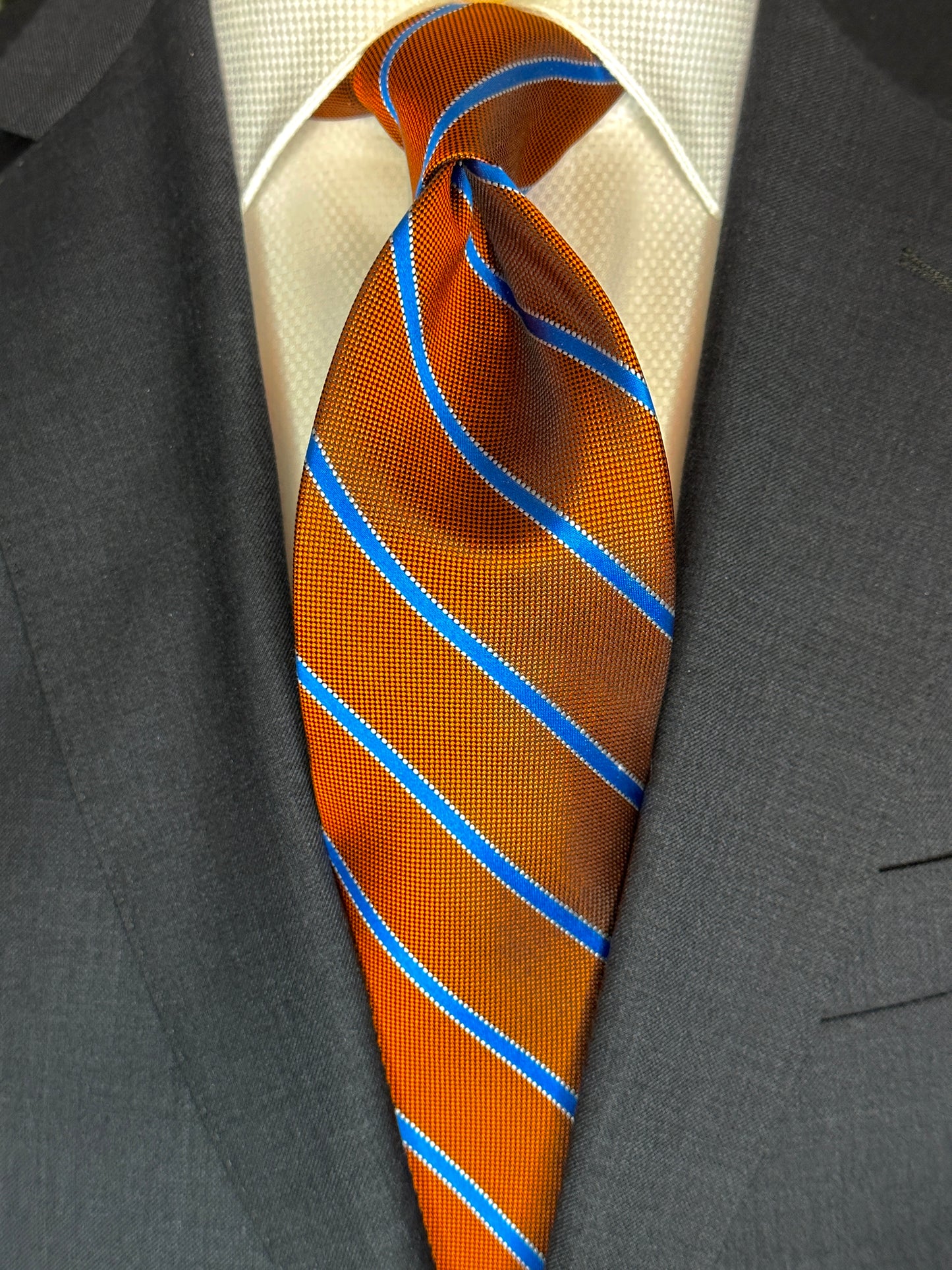 This beautiful burnt orange woven silk necktie is a stunning rich color with a baby blue stripe running through it. A perfect tie for any season and matching with a multitude of suit colors and patterns, this is a very versatile tie. In Italy, the mini plaid shirt with striped tie is a sophisticated ensemble. 