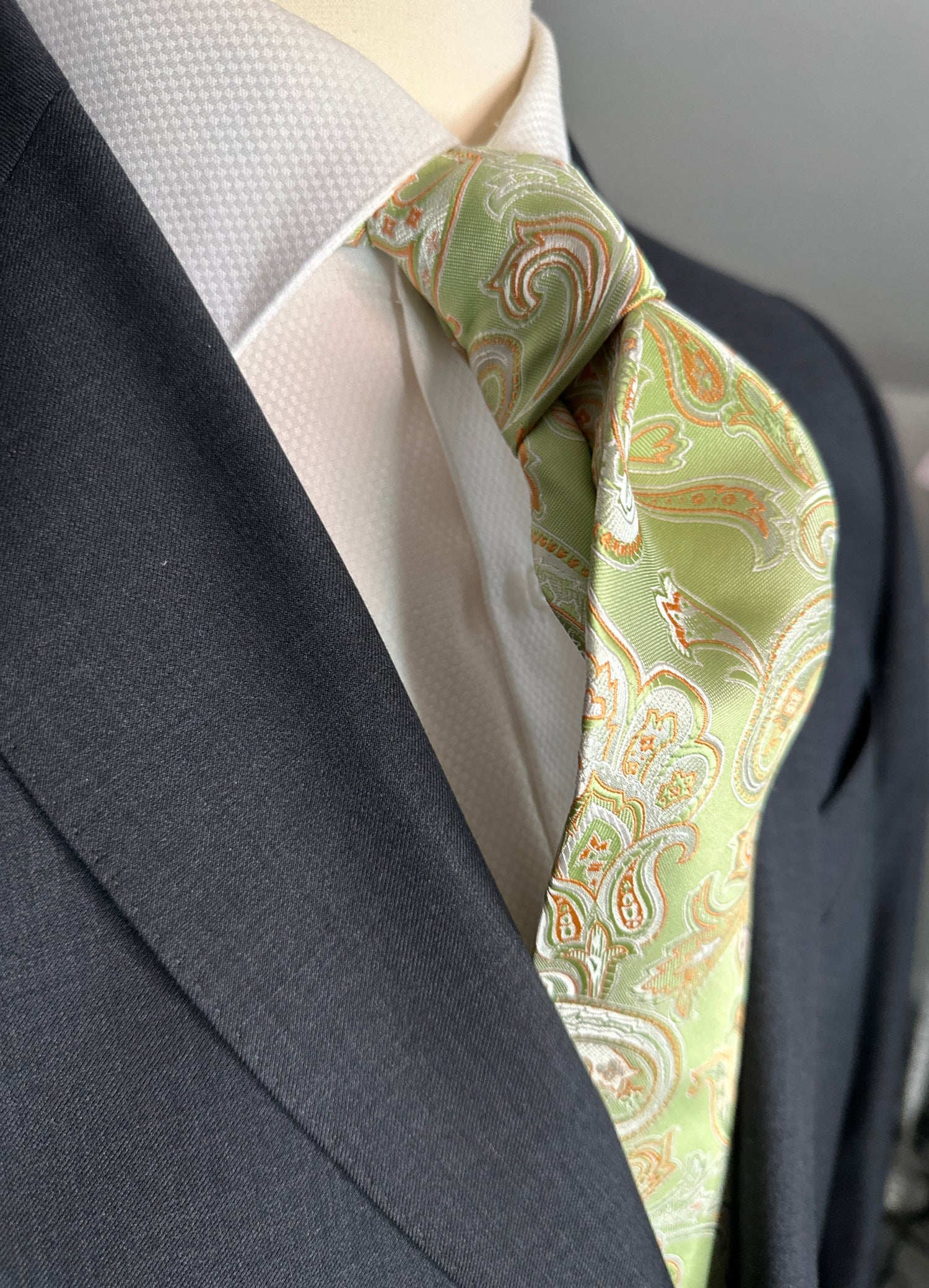 This 100% silk woven tie has a beautiful large paisley pattern in pale orange and beige on a pale green background. Great to use with light colorations in shirts and clothing for spring summer occasions. Suits in light blue, olive green, and summer tan will go best with this tie. Don't forget about the navy blazer.