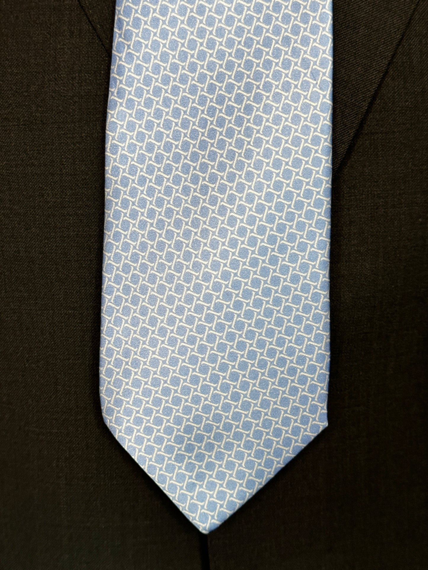 This satin finish 100% silk necktie has a very interesting all over geometric pattern of interlocking white links almost chain link in style. The silk is very smooth to the touch and has a natural luster that shines in certain light. This is a serious tie. Great for those business meetings, court dates, daytime or evening events, and all around more formal attire. This is best paired with a fancy white or tone on tone white dress shirt.