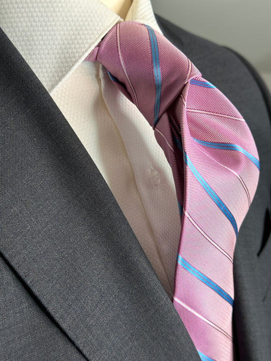 This pale pink woven silk necktie has two different types of silk. The blue stripes are satin silk with the broad stripes in 100% woven silk. Easily used on a sky blue shirt with a multiple array of different suit colors, this tie fits well for daytime and evening time use.