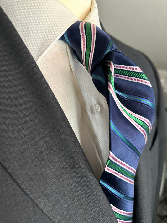 A multistripe tie has many functions. This 100% silk navy blue base tie has multiple types of stripes running through it. Light blue, rose, white ands green impact this toe in different widths. The multistripe tie allows for many types of colorations and patterns in shirts and suits. Probably the most versatile. 