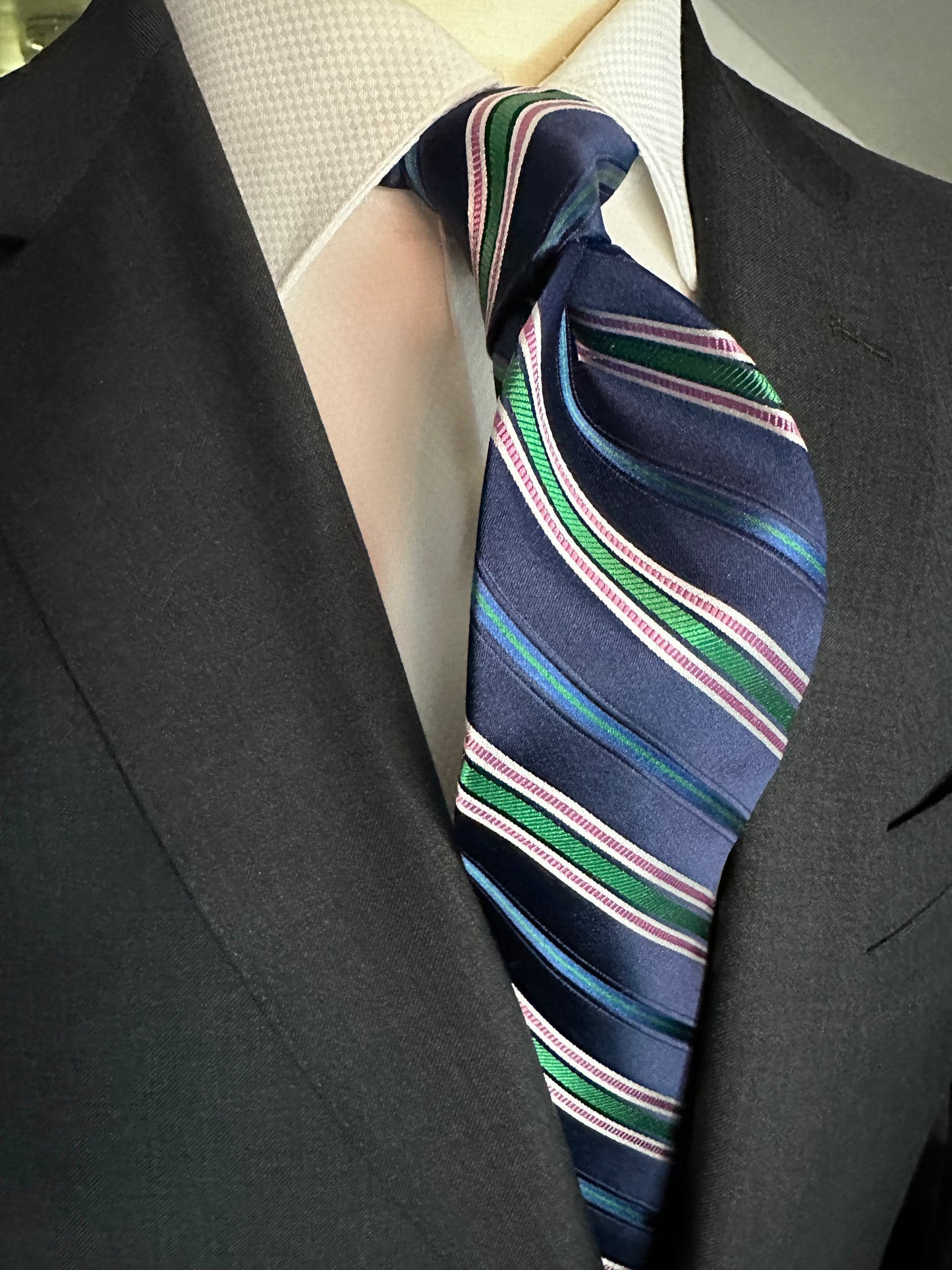 A multistripe tie has many functions. This 100% silk navy blue base tie has multiple types of stripes running through it. Light blue, rose, white ands green impact this toe in different widths. The multistripe tie allows for many types of colorations and patterns in shirts and suits. Probably the most versatile. 