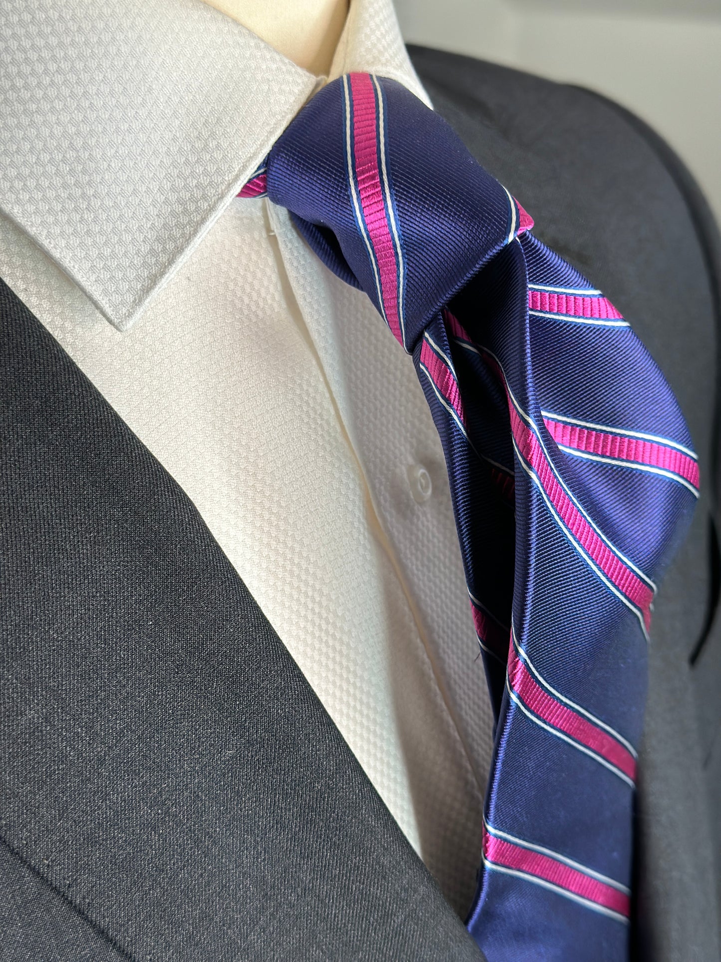 100% silk necktie in classic navy blue background with a stunning woven silk pink stripe. This tie is fantastic with the classic suits of navy, charcoal grey and pinstripes. Excellent with a crisp white french cuff shirt. 