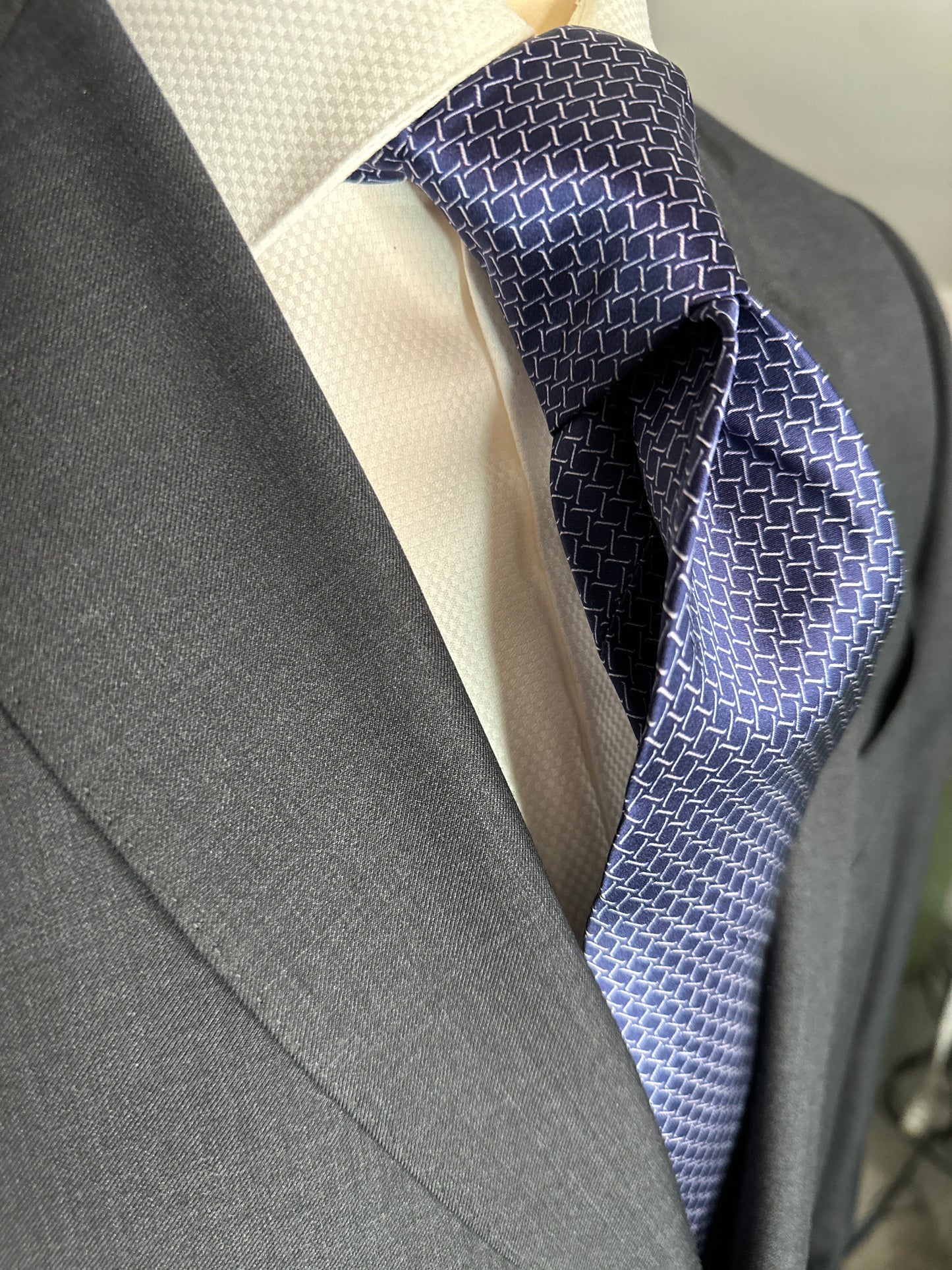 This satin finish 100% silk necktie has a very interesting all over geometric pattern of interlocking white links almost chain link in style. The silk is very smooth to the touch and has a natural luster that shines in certain light. This is a serious tie. Great for those business meetings, court dates, daytime or evening events, and all around more formal attire. This is best paired with a fancy white or tone on tone white dress shirt.