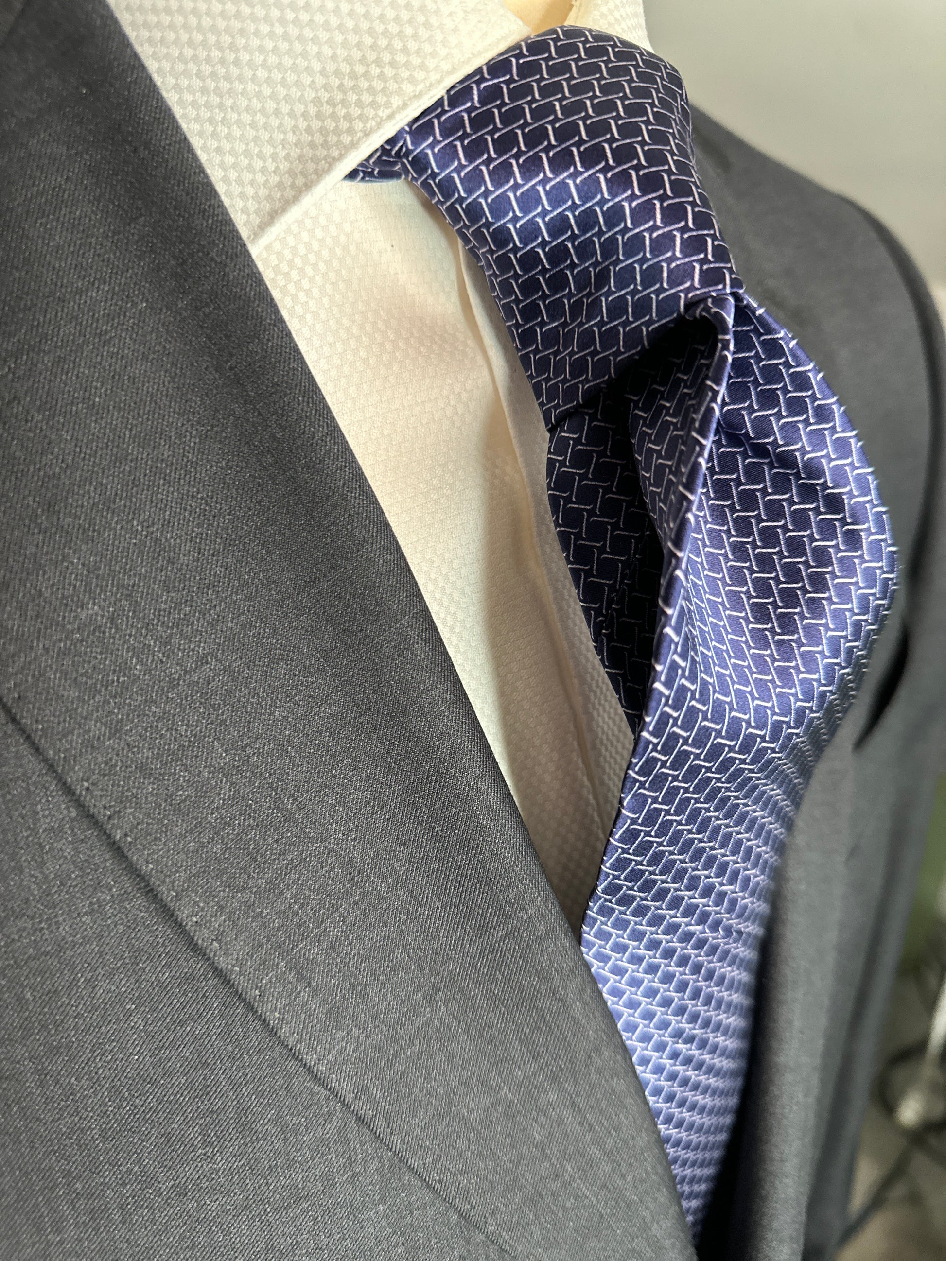 This satin finish 100% silk necktie has a very interesting all over geometric pattern of interlocking white links almost chain link in style. The silk is very smooth to the touch and has a natural luster that shines in certain light. This is a serious tie. Great for those business meetings, court dates, daytime or evening events, and all around more formal attire. This is best paired with a fancy white or tone on tone white dress shirt.