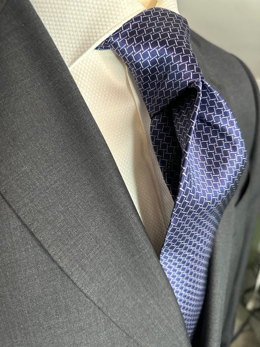 This satin finish 100% silk necktie has a very interesting all over geometric pattern of interlocking white links almost chain link in style. The silk is very smooth to the touch and has a natural luster that shines in certain light. This is a serious tie. Great for those business meetings, court dates, daytime or evening events, and all around more formal attire. This is best paired with a fancy white or tone on tone white dress shirt.