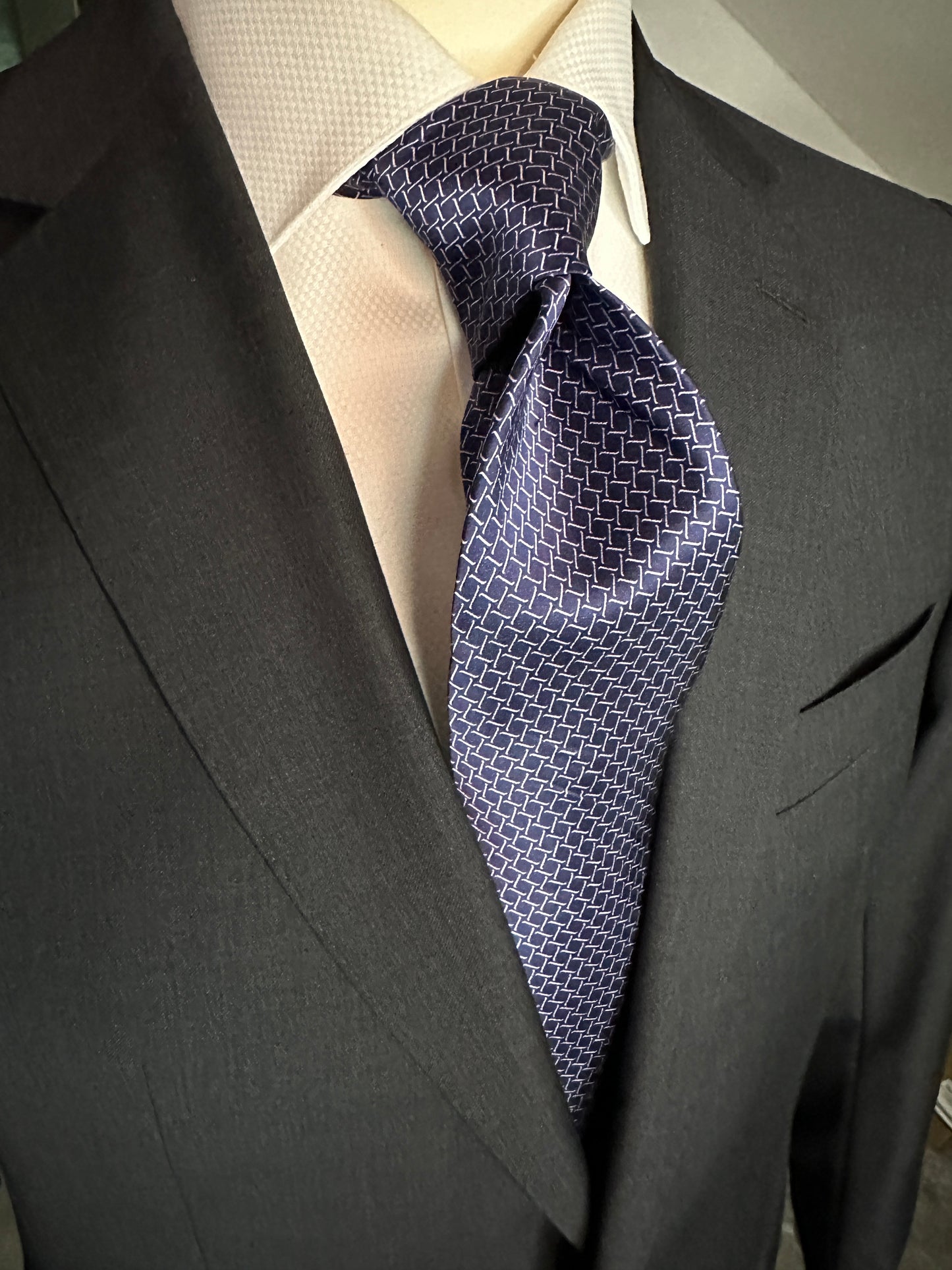 This satin finish 100% silk necktie has a very interesting all over geometric pattern of interlocking white links almost chain link in style. The silk is very smooth to the touch and has a natural luster that shines in certain light. This is a serious tie. Great for those business meetings, court dates, daytime or evening events, and all around more formal attire. This is best paired with a fancy white or tone on tone white dress shirt.