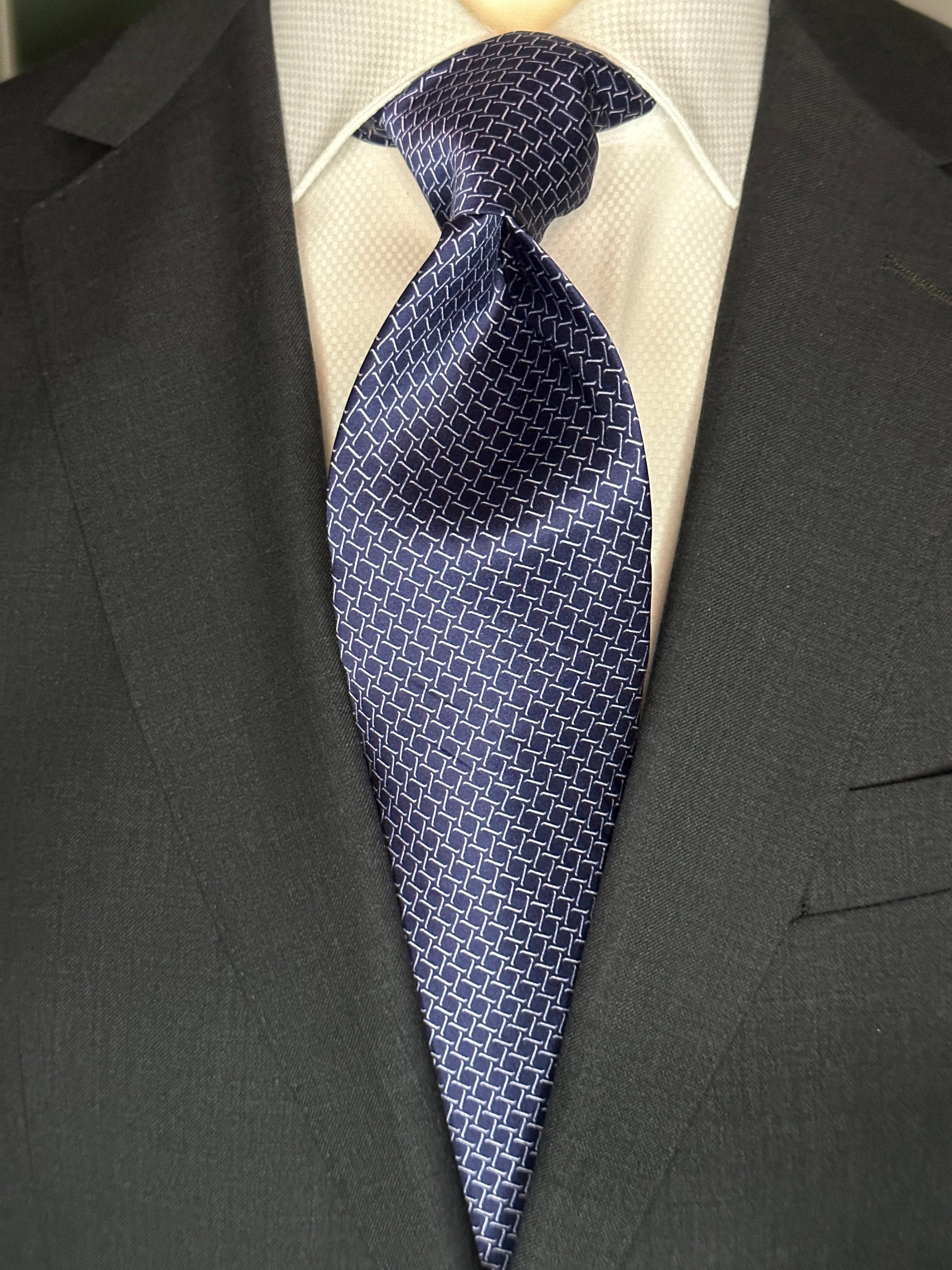 This satin finish 100% silk necktie has a very interesting all over geometric pattern of interlocking white links almost chain link in style. The silk is very smooth to the touch and has a natural luster that shines in certain light. This is a serious tie. Great for those business meetings, court dates, daytime or evening events, and all around more formal attire. This is best paired with a fancy white or tone on tone white dress shirt.