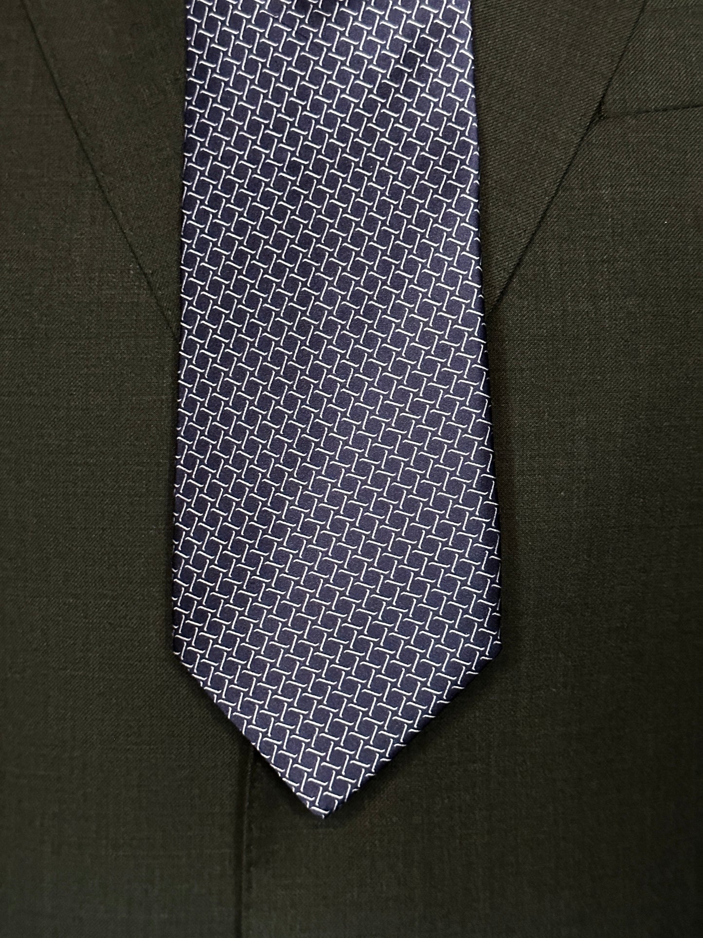 This satin finish 100% silk necktie has a very interesting all over geometric pattern of interlocking white links almost chain link in style. The silk is very smooth to the touch and has a natural luster that shines in certain light. This is a serious tie. Great for those business meetings, court dates, daytime or evening events, and all around more formal attire. This is best paired with a fancy white or tone on tone white dress shirt.