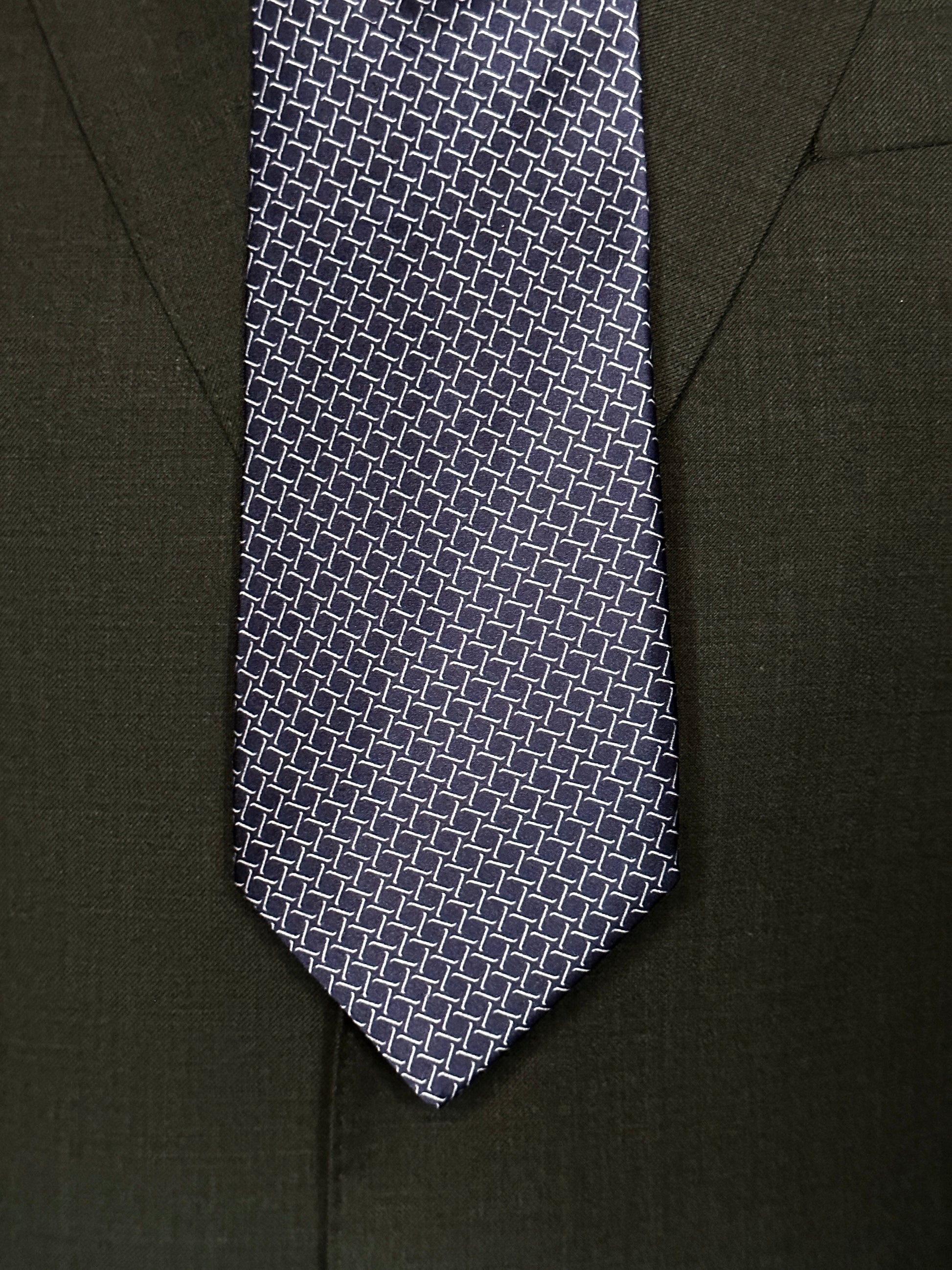 This satin finish 100% silk necktie has a very interesting all over geometric pattern of interlocking white links almost chain link in style. The silk is very smooth to the touch and has a natural luster that shines in certain light. This is a serious tie. Great for those business meetings, court dates, daytime or evening events, and all around more formal attire. This is best paired with a fancy white or tone on tone white dress shirt.