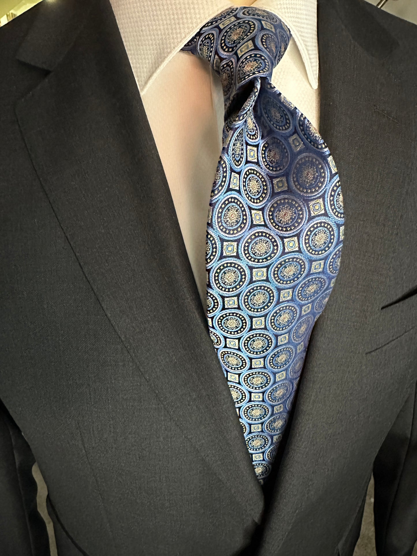 This 100% woven silk tie has a gorgeous weight and thickness to the finish. With woven medallions in shades of blue and taupe, this is a necktie that makes a statement. To be worn with shirts in white, blue, beige and grey. This tie also pairs well with shirts with small plaids and mini checks. See the sister color in purple.