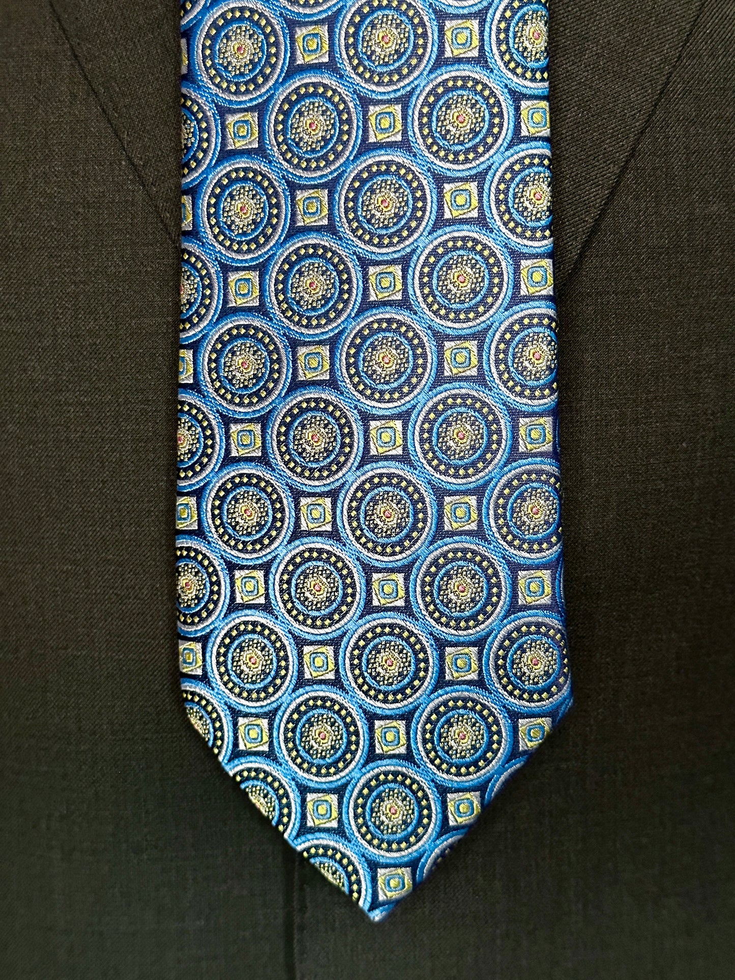 This 100% woven silk tie has a gorgeous weight and thickness to the finish. With woven medallions in shades of blue and taupe, this is a necktie that makes a statement. To be worn with shirts in white, blue, beige and grey. This tie also pairs well with shirts with small plaids and mini checks. See the sister color in purple.