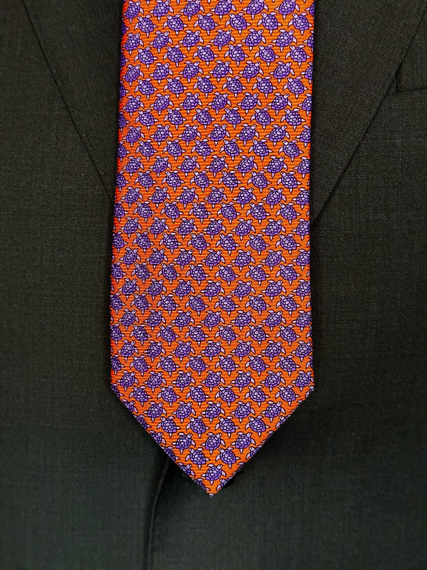 A tie with turtles, what could be better? You don't see turtles? This beautiful geometric pattern is made of closely bunched turtles in purple against an orange background. What is so great about this tie is that from afar this necktie is a neat pattern, but as you get closer it can be seen there are small turtles together. Hermes style. 