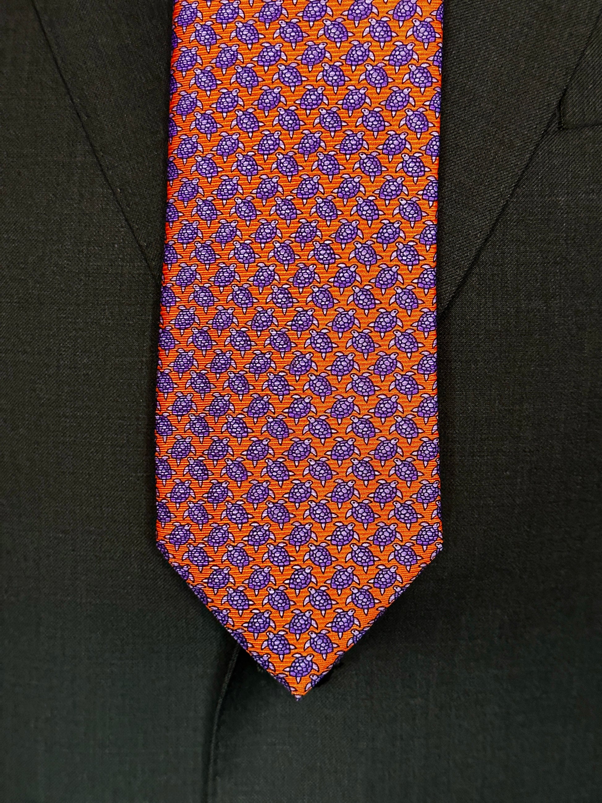 A tie with turtles, what could be better? You don't see turtles? This beautiful geometric pattern is made of closely bunched turtles in purple against an orange background. What is so great about this tie is that from afar this necktie is a neat pattern, but as you get closer it can be seen there are small turtles together. Hermes style. 