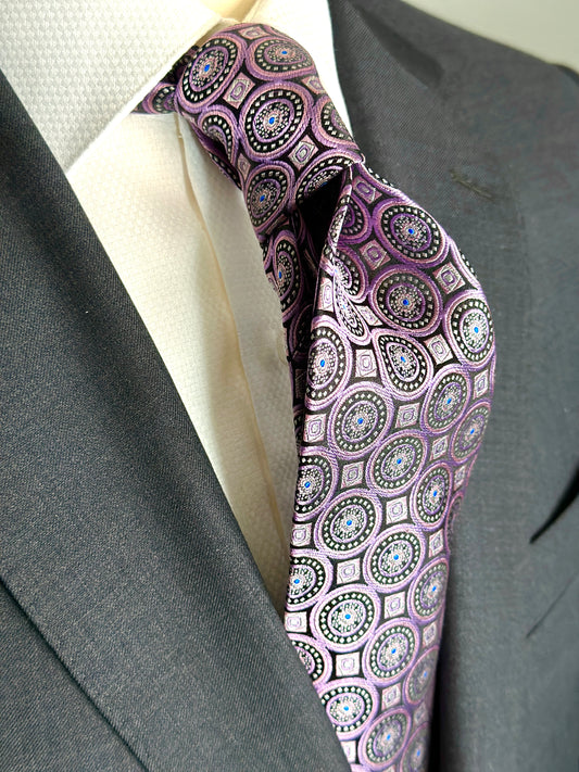 SUITCAFE This 100% woven silk tie has a gorgeous weight and thickness to the finish. With woven medallions in shades of purple and black, this is a necktie that makes a statement. To be worn with shirts in white, blue, pink, beige and grey. This tie also pairs well with shirts with small plaids and mini checks. See the sister color in blue.