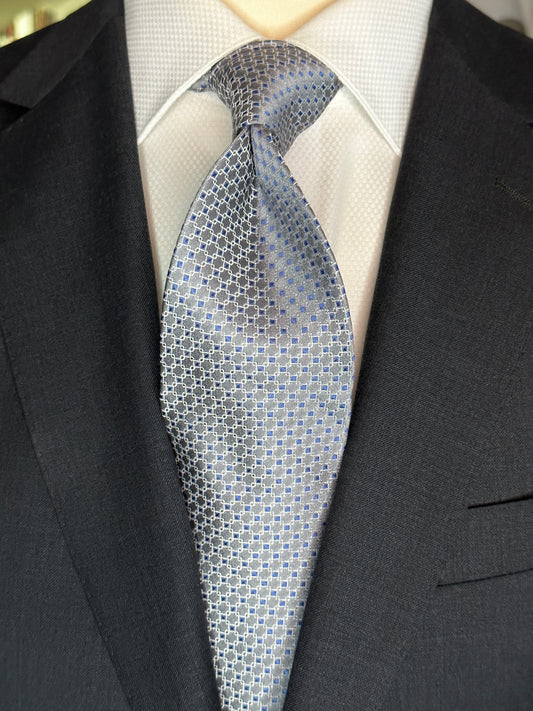 This 100% silk necktie is made from the finest Italian woven silk. The pattern is a small neat geometric making for a cool, crisp look. Inside each small checkered square is a small royal blue dot. This is a very sophisticated tie for business, dinners or even a wedding.