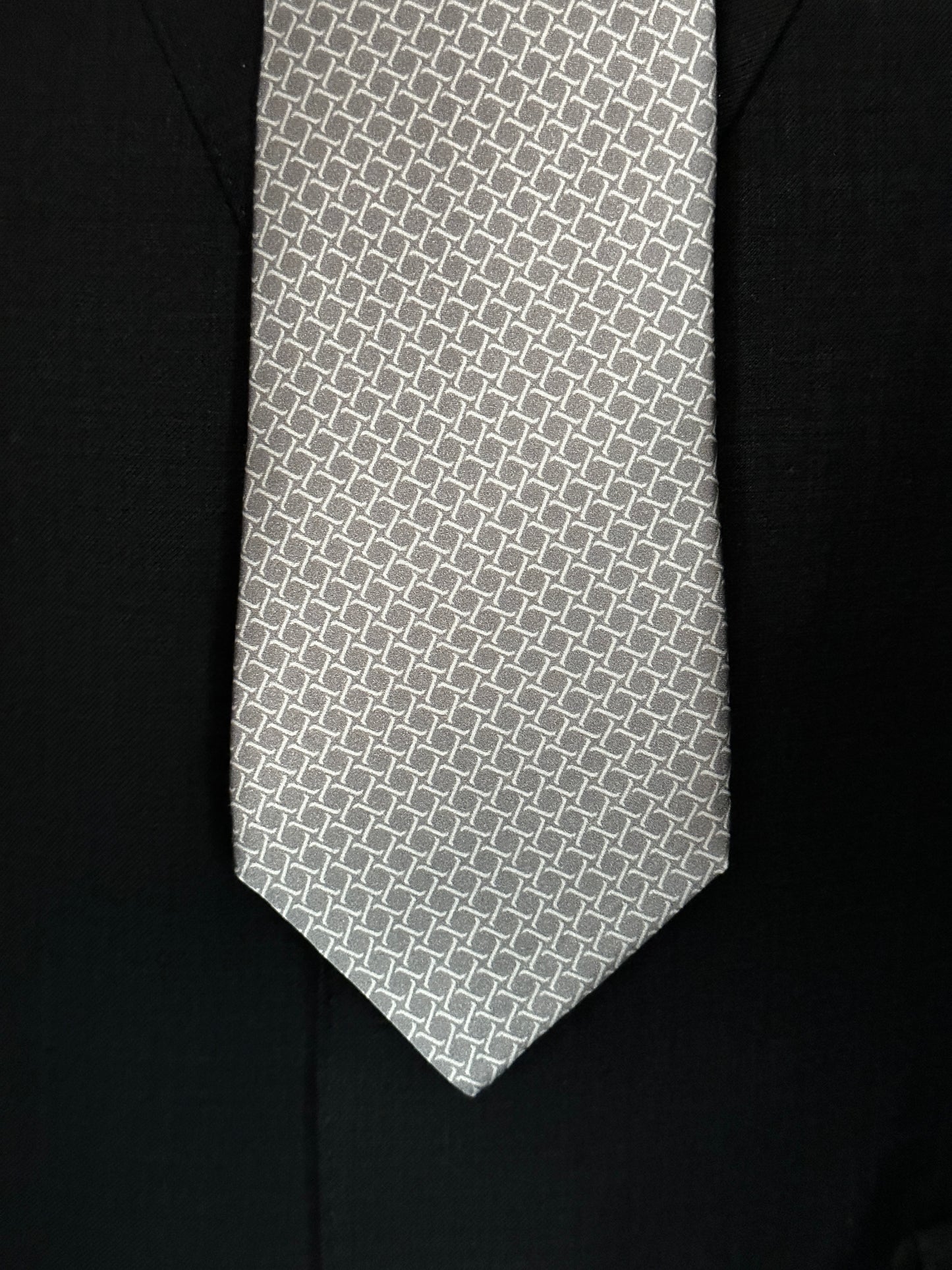 This satin finish 100% silk necktie has a very interesting all over geometric pattern of interlocking white links almost chain link in style. The silk is very smooth to the touch and has a natural luster that shines in certain light. This is a serious tie. Great for those business meetings, court dates, daytime or evening events, and all around more formal attire. This is best paired with a fancy white or tone on tone white dress shirt.