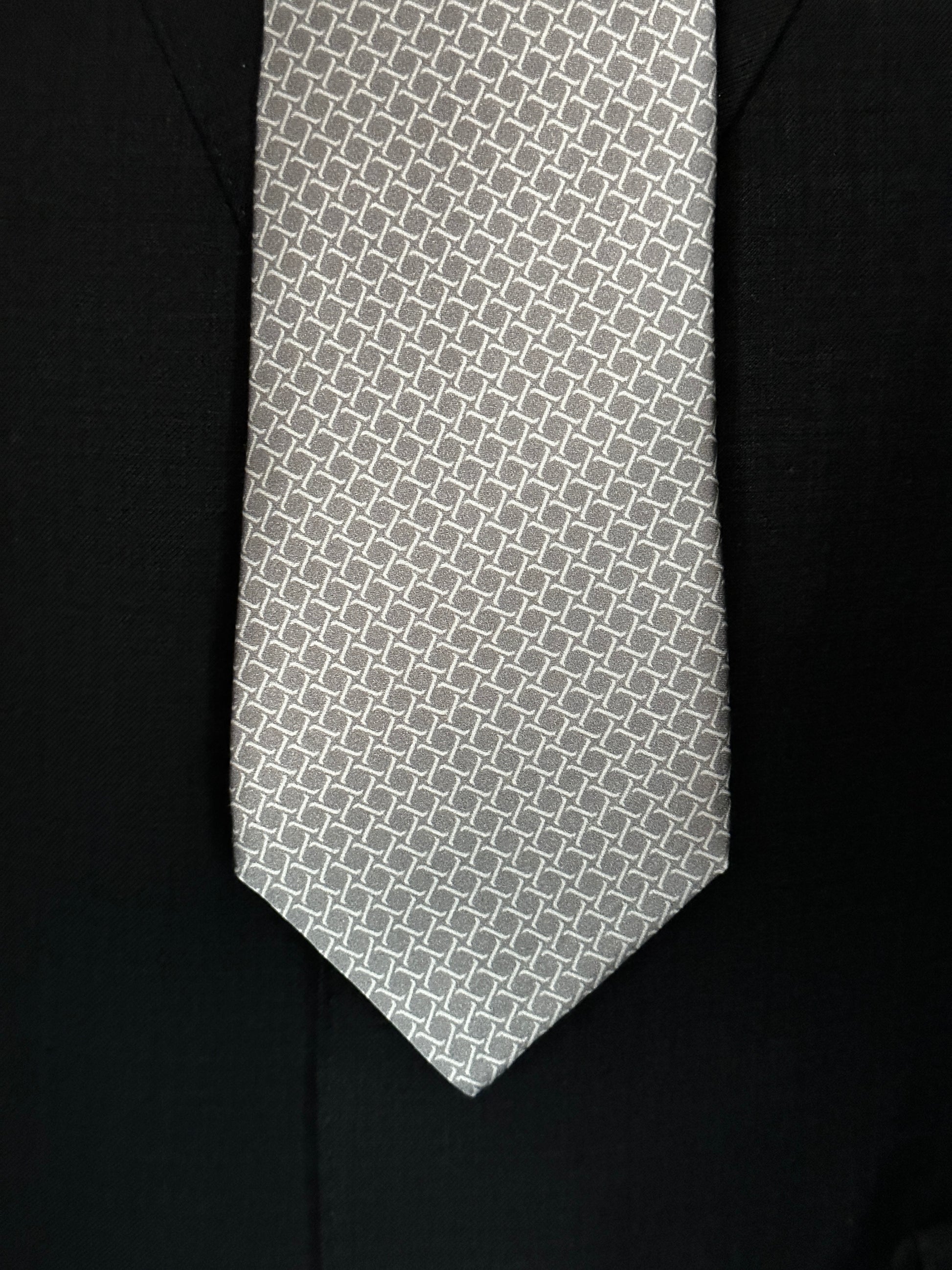 This satin finish 100% silk necktie has a very interesting all over geometric pattern of interlocking white links almost chain link in style. The silk is very smooth to the touch and has a natural luster that shines in certain light. This is a serious tie. Great for those business meetings, court dates, daytime or evening events, and all around more formal attire. This is best paired with a fancy white or tone on tone white dress shirt.